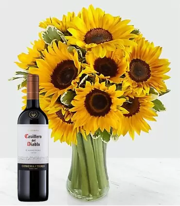 Florero con 10 girasoles acompañado de una botella de vino tinto.