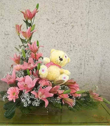 Arreglo Ikebana rosado con 8 liliums, 7 gerberas y osito peluche para nacimiento de niña.